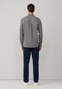 Camisa gris de manga larga, ajustada, con un pliegue en la parte posterior, combinada con pantalones azul marino y zapatillas blancas. Diseño minimalista.