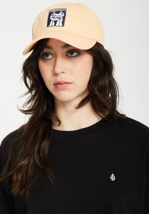 Peach-colored cap with a black embroidered graphic, worn with a plain black t-shirt. The cap features a curved brim and adjustable back.