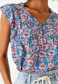 Blouse fleurie en rose, bleu et jaune avec manches à volants, encolure en V, boutons et motif complexe sur un tissu léger.