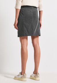 Jupe en coton gris à coupe droite, avec une fente à l'arrière et une taille simple. Portée avec des baskets de couleur claire. Texture lisse, sans motifs visibles.