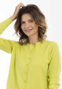Cardigan leggero verde lime, con scollatura rotonda, chiusura a bottoni e polsini a costine. Tessuto morbido e texture liscia.