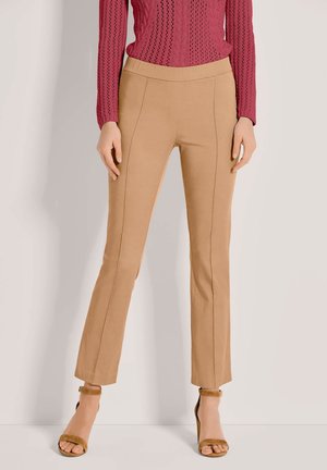 Beige, ausgestellt geschnittene Hosen mit glatter Textur, elastischem Bund und kontrastierenden Nähten. Kombiniert mit braunen High-Heels.