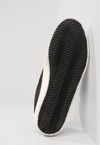 Sole di sneaker in bianco e nero con una superficie in gomma testurizzata, caratterizzata da un motivo a zigzag e accenti laterali lisci.