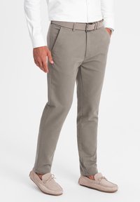 Pantalons beige ajustés avec une coupe droite, en tissu mélangé coton, avec un pli marqué, et une ceinture assortie. Associés à des mocassins beiges.