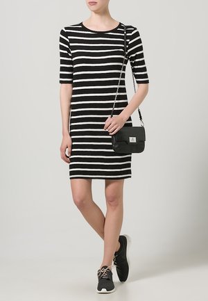 Nainen, jolla on mustavalkoinen vaakaraitainen mekko, mustat tennarit ja pieni musta ristiselkälaukku ketjuhihnalla.