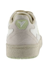 Sneaker bianca con accenti beige testurizzati, suola testurizzata e logo esagonale verde chiaro sul tallone. Lacci rotondi e design a profilo basso.