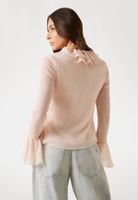 Ljusrosa blus med volangkrage och trumpetärmar, i ett texturerat tyg. Bärs med högmidjade ljusa jeans.