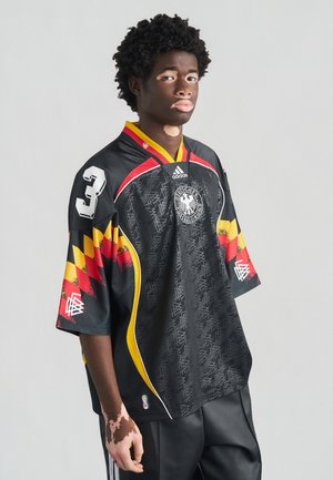 Maglia nera con dettagli gialli, rossi e decorati, presenta un grande numero "3" e uno stemma ricamato. Realizzata in tessuto leggero.