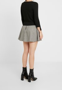 Svart figurnära långärmad topp i kombination med en plisserad minikjol i svart och vit rutig mönster samt svarta klackstövlar som når ankeln.
