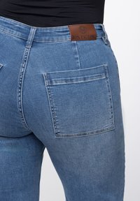 Helle blaue Jeans mit hoher Taille, ausgestattet mit einem Lederlogo-Patch auf der Rückseite und einer Gesäßtasche auf der rechten Seite.