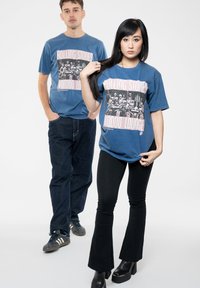 Graphic t-shirts in faded blue featuring a black and pink Rolling Stones "Voodoo Lounge" design, paired with dark jeans and flared pants.