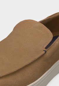 Ταν σουέντ παπούτσι τύπου slip-on με λευκή σόλα από καουτσούκ και ελάχιστη ραφή στο επάνω μέρος.