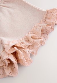 Tissu en coton rose clair avec bordure volant en dentelle ; le volant présente des trous découpés au laser créant un motif délicat le long du bord.