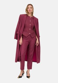 Fuchsienfarbenes Wollmisch-Anzug mit tailliertem Schnitt, bestehend aus einem doppelt geknöpften Sakko, schlanken Hosen und einem langen Mantel mit kontrastierendem Innenfutter.