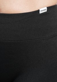 Ceinture côtelée noire avec une petite étiquette blanche affichant "SMILODOX". Le matériau semble doux et élastique, avec une texture lisse.