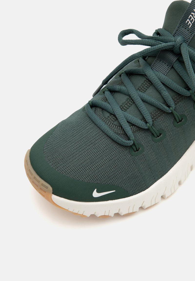 Zielony tekstylny sneaker z zaokrąglonym noskiem, białą podeszwą i kontrastującymi szarymi akcentami. Posiada sznurówki i małe białe logo.