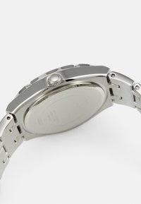 Orologio in acciaio inossidabile argentato con cassa rotonda, corona texturizzata e bracciale a maglie metalliche. Retro liscio con dettagli di branding minimali.