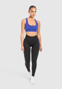 Blå sport-bh och svarta högmidjade leggings i stretchmaterial. Vita sportskor. Enkelt mönster, slät textur, inga mönster.