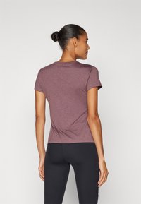 Kortermet, tettsittende T-skjorte i en dyp mauve-farge, laget av mykt, teksturert stoff. Designet med en klassisk rund hals og en diskret buet kant.