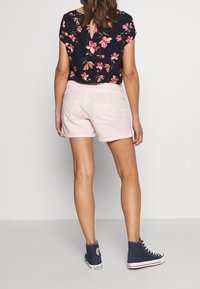 Blusa floreale blu navy con maniche corte e dettaglio a chiave sul retro abbinata a pantaloni corti rosa chiaro e sneakers alte blu scuro.