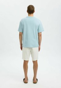 Ljusblå kortärmad t-shirt i mjukt tyg, kombinerad med vita shorts. Bakifrån visar den en avslappnad passform och en enkel design.