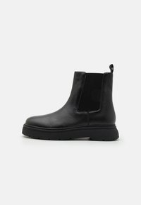 Bottines en cuir noir avec un panneau latéral élastique côtelé, bout rond et semelle épaisse noire. Comprend une languette à l'arrière pour faciliter l'enfilage.