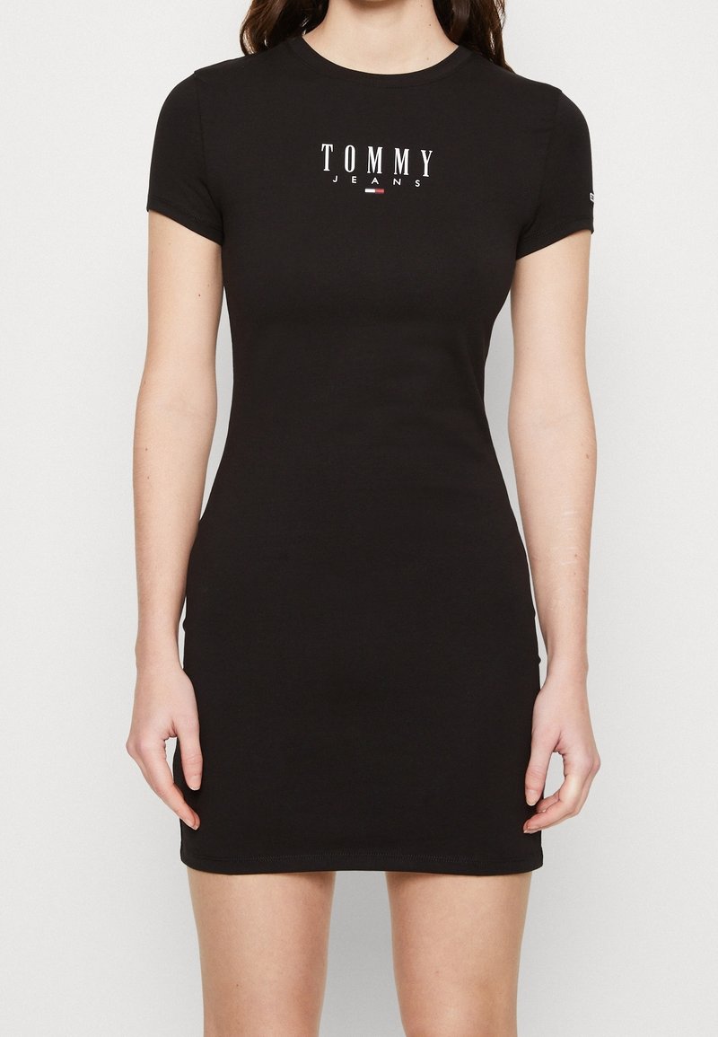 Černé přiléhavé šaty s krátkým rukávem vyrobené z bavlny, s bílým logem "TOMMY JEANS" tištěným na hrudi a kulatým výstřihem.