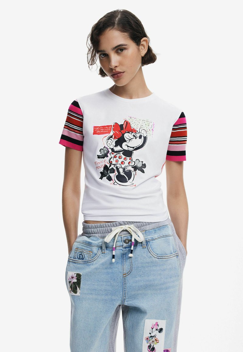 White T-shirt featuring a graphic of Minnie Mouse, with pink accents on striped sleeves. Paired with light blue denim pants displaying floral patches.