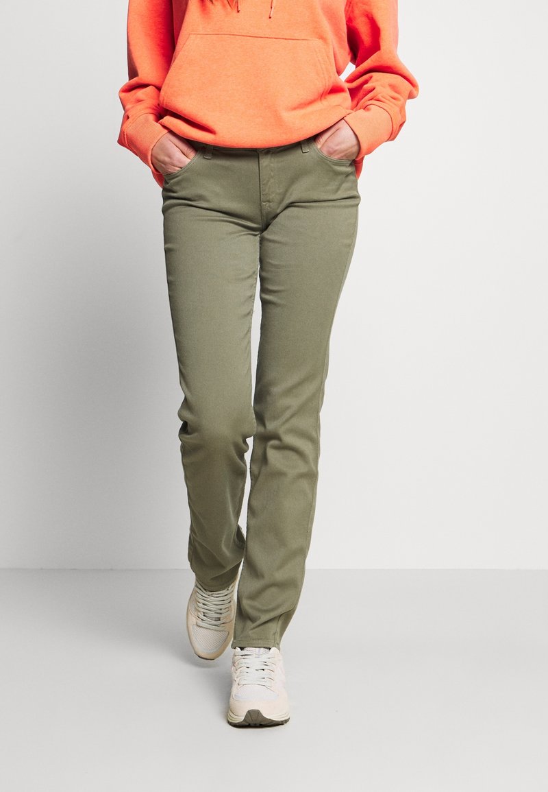 Pantalons vert olive slim, dotés de cinq poches et d'une taille mi-haute, associés à un hoodie orange vif et des baskets claires.