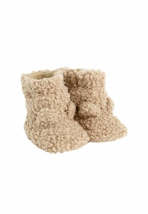 Chaussons pour bébé en beige pelucheux avec un design texturé et bouclé.  orteils arrondis et doublure intérieure douce, présentant un détail décoratif en pompon.