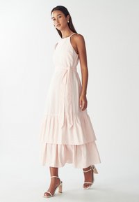 Vestido midi a rayas en rosa suave con un corpiño ajustado, falda de volantes en capas y cinturón de cinta. Presenta tirantes finos y una silueta relajada.