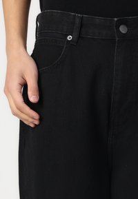 Black denim jeans with a straight cut, featuring a button and zipper closure, five-pocket design, and contrast stitching.