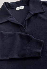 Tengerészkék polóing bordázott textúrával, puha gallérral és hosszú ujjakkal. A címke felirata: "Next Maternity".