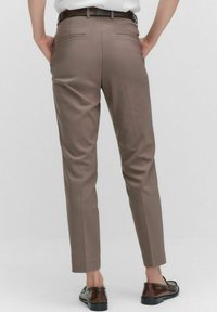 Brown tailored pants with a smooth texture, slim fit and two rear pockets. Worn with a white shirt and black shoes.