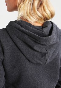 Sweat à capuche gris foncé, doté d'une capuche à double épaisseur, d'une texture de tissu douce et d'une coupe décontractée. Coutures visibles au niveau de l'encolure.