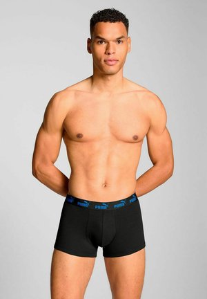 Black boxer briefs with a blue Puma logo band, cotton material, fitted shape, and smooth texture. Model stands with arms behind back.