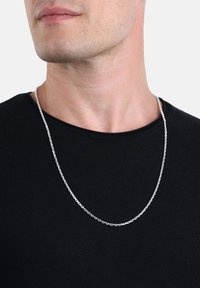 Silver kedja hängsmycke visat på en modell, med en enkel länkdesign. Bärs över en svart crew-neck tröja. Slät textur, standard längd.