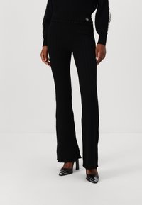 Pantaloni negri evazați cu căptușeală texturată la talie și detalii decorative. Asociați cu pantofi cu toc înalt, negri și strălucitori.