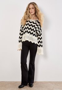 Schwarzer und weißer zwiebelmuster Pullover mit einem gewellten Saum, kombiniert mit schwarzen Schlaghosen und schwarzen Schuhen. Weiches, gestricktes Material.