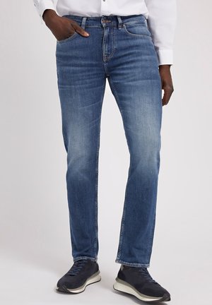 Jeans en denim de lavage bleu moyen, coupe slim avec un léger délavage. Comprend cinq poches, une fermeture éclair et une taille standard.