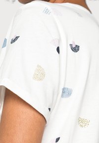 Camiseta blanca de manga corta con formas y patrones abstractos multicolores. El material es algodón suave con un acabado texturizado.