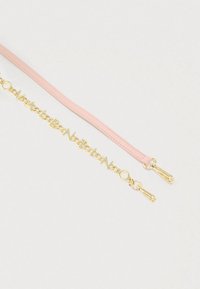 Két szemüveglánc fehér felületen, az egyik rózsaszín bőrből, a másik aranyszínű fém betűkből álló mintát alkot.