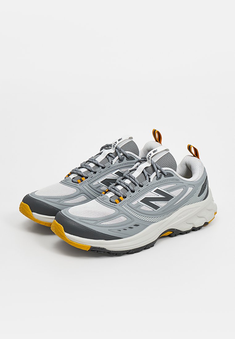Par de zapatillas deportivas grises y blancas con detalles en negro y amarillo, cordones atados y suelas acolchadas sobre un fondo liso.