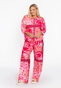 Roze en rode florale print co-ord set met een knoopsluiting shirt en wijde broek, met gedurfde strepen en een lichtgewicht, gladde stoftextuur.