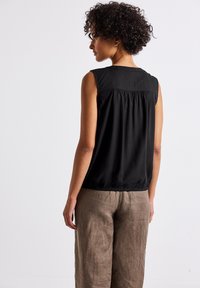 Top sans manches noir avec un détail froncé au dos, un col rond et une taille élastique. Associé à un pantalon en lin beige clair, ample.