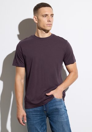 Kurzärmeliges, Rundhals-T-Shirt aus dunklem lila Baumwollstoff; kombiniert mit blauen Denim-Jeans, die eine entspannte Passform und glatte Textur aufweisen.