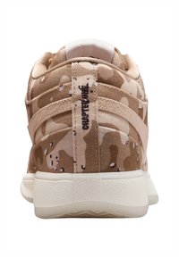 Beige stoffen sneakers met een camouflagemotief, een getextureerd oppervlak, een witte zool en contrasterende merkopdruk op de hiel.