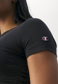 Czarny dopasowany t-shirt z krótkimi rękawami, wykonany z materiału o subtelnej prążkowanej fakturze, z małym haftowanym logo na lewym rękawie.