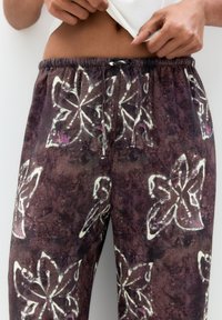Pantaloni in tessuto marrone con un motivo floreale bianco e accenni di viola, dotati di una vita elastica e dettaglio con coulisse.