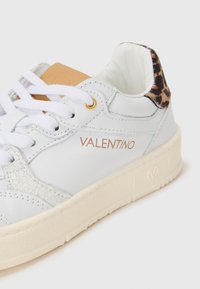 Sneaker bianco in pelle con pannello grigio testurizzato, occhielli dorati e un accento a stampa leopardata sul tallone. Presenta chiusura con lacci e suola spessa.